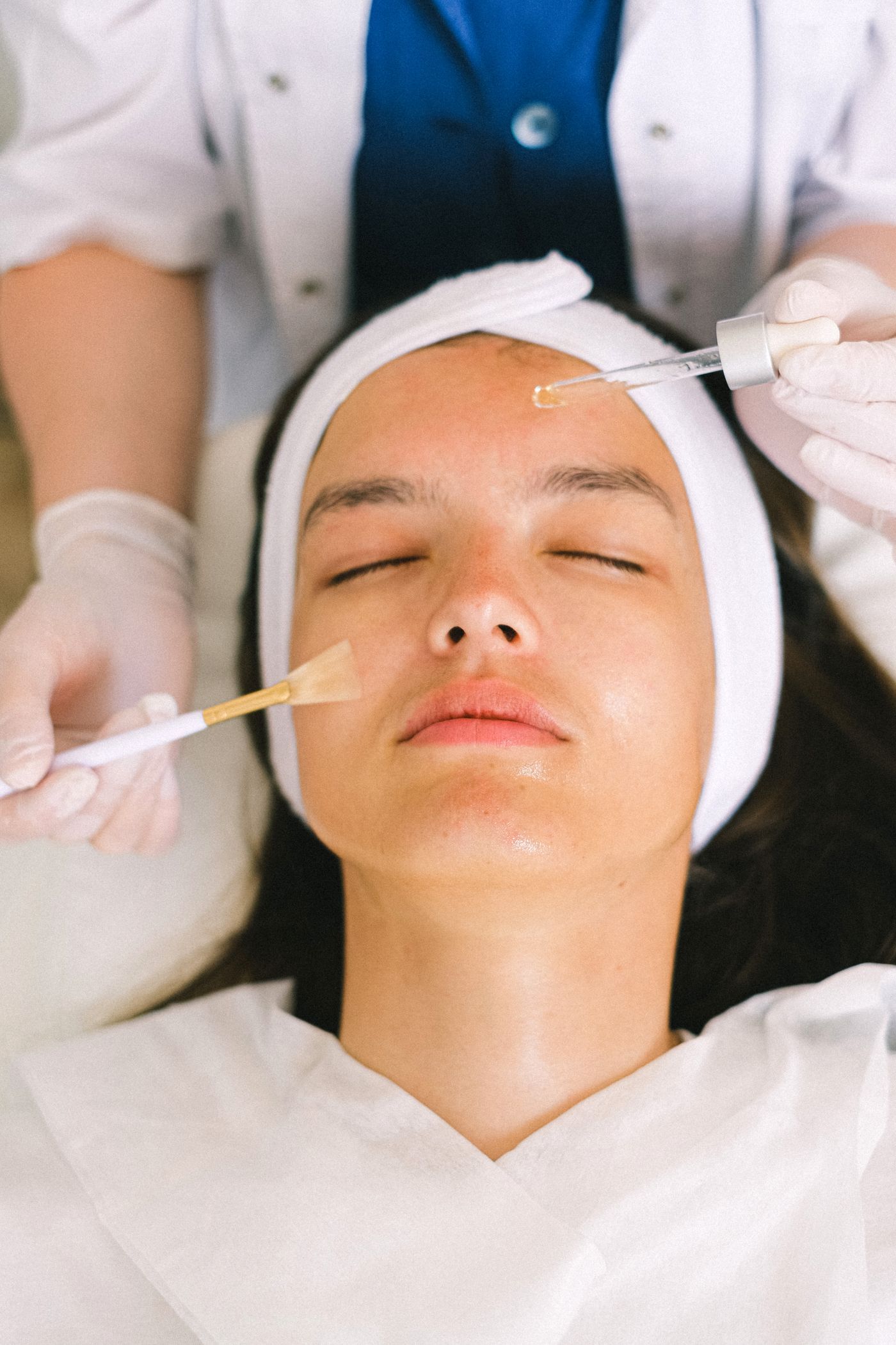Esthetician applying product to a client's face with a brush and dropper